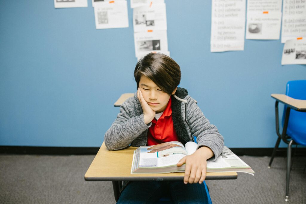 pexels-photo-6936387-6936387 A young boy deep in thought while reading a book alone in a classroom.